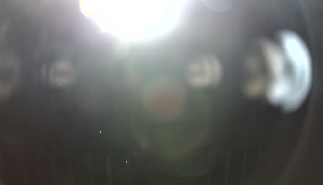 A bright light source is present in the top right corner, causing a glare that obscures much of the image. There are blurred circular shapes and reflections visible, while the background appears dark and indistinct.