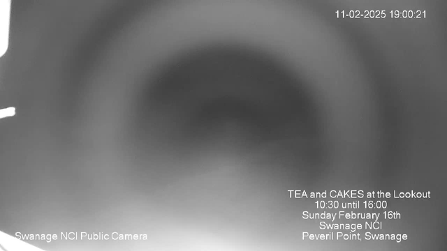 A blurred webcam image showing a gradient from dark to light, with text overlaid in the lower part of the image. The text announces an event for tea and cakes at the Lookout in Swanage, with the date and time listed, as well as the location, Peveril Point, Swanage. The clarity of the image is low, making it difficult to discern specific details in the background.