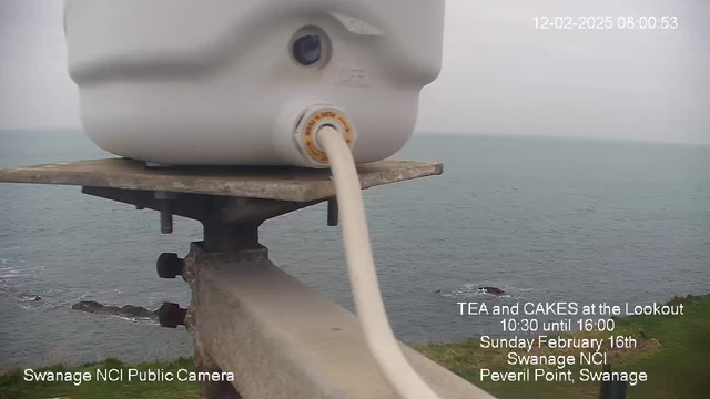 A close-up view of a white cylindrical object attached to a metal platform, with a thin white tube extending from it. In the background, a cloudy sky transitions to a gray sea, with rocky formations visible along the coastline. Text on the image promotes an event for tea and cakes at Swanage NCI on February 16th.