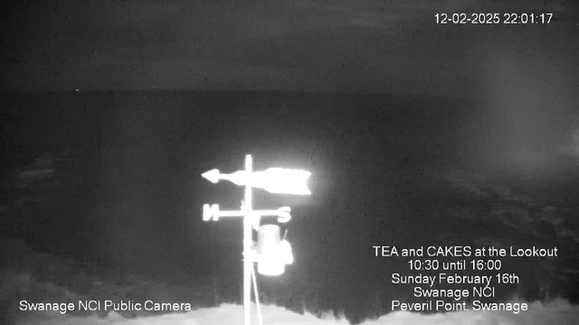 A dark evening scene over the ocean, with a faint horizon line visible. A weather vane is centered in the foreground, indicating the cardinal directions—north is at the top, south at the bottom, with arrows pointing towards east and west. Text on the image mentions a tea and cakes event at Swanage NCI on February 16th, including the time and location details. The image has a grainy, monochrome quality.