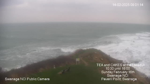 An overcast seascape showing turbulent sea waves crashing against the shore. The foreground features patchy grass and some rocky outcrops. In the distance, the horizon meets a cloudy sky, giving the impression of an early morning with muted light. Text in the corner promotes an event at Swanage NCI with information about tea and cakes. A bench is visible on the grassy area near the edge. The overall mood is tranquil yet dramatic due to the choppy waters.