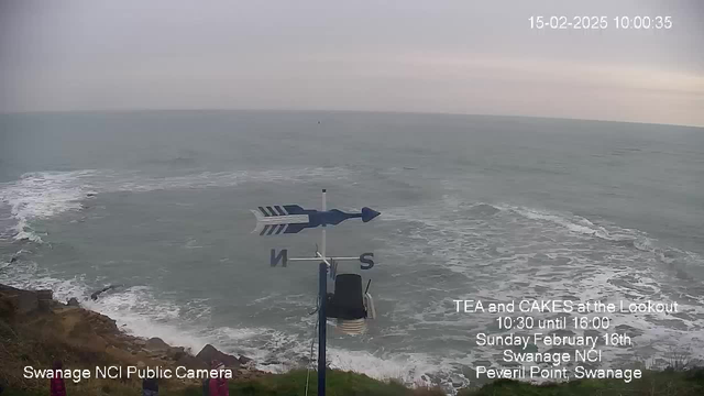 A cloudy seaside scene showing gentle waves lapping against a rocky shoreline. In the foreground, a blue and white weather vane is visible, indicating directions with "N" for north prominently displayed. The text at the bottom promotes an event for tea and cakes, providing details about the time and location: Peveril Point, Swanage. The overall atmosphere is calm and tranquil, with muted colors reflecting an overcast sky.