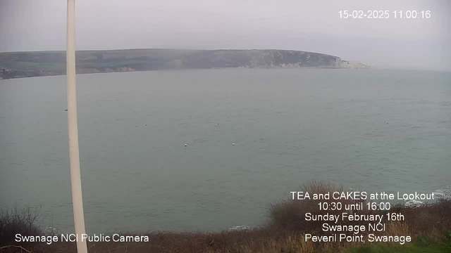 A coastal view featuring calm, greenish water extending to the horizon under an overcast sky. In the distance, there are cliffs with patches of greenery. A white pole is visible in the foreground on the left side. Informational text in the bottom right corner highlights an event, reading "TEA and CAKES at the Lookout" with details about the date and location in Swanage.