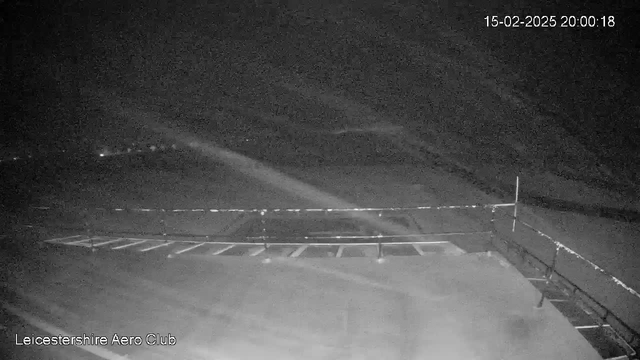 A dimly lit scene from a webcam at Leicestershire Aero Club, showing a runway area with faint outlines of the runway markings. The background appears to be mostly dark, with some indistinct lights in the distance. The timestamp in the corner indicates the date and time as February 15, 2025, at 20:00:18.