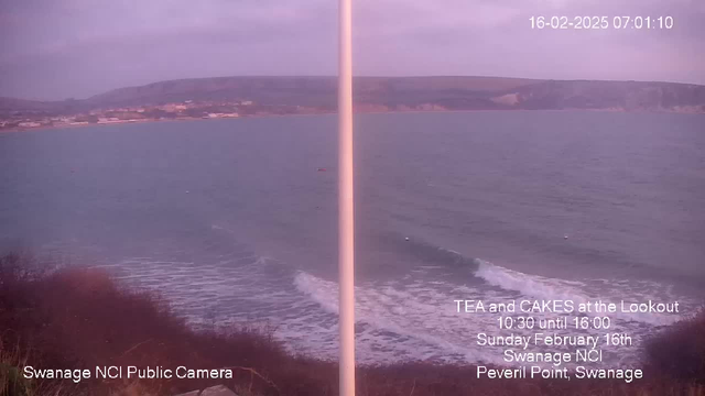 A coastal scene featuring calm waters and gentle waves lapping at the shore. In the background, there are rolling hills and some buildings along the coastline. The sky is overcast, giving the image a soft, muted light. A white pole stands prominently in the foreground, partially obscuring the view. Text in the lower right corner indicates an event for tea and cakes at a lookout, along with the date and location details.