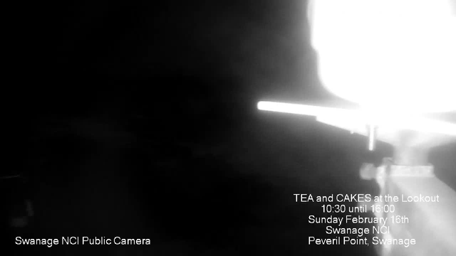 A dark image with minimal visibility, featuring a bright white area in the upper right corner, suggesting a light source or object in focus. Text at the bottom left indicates "Swanage NCI Public Camera." The lower right corner contains event details with white text on a black background, announcing "TEA and CAKES at the Lookout," the date "Sunday February 16th," and location information "Swanage NCI, Peveril Point, Swanage." The overall image has a grainy quality, possibly due to low light conditions.