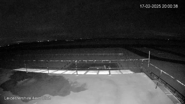 A dark scene captured from a webcam at Leicestershire Aero Club. The image shows a runway and surrounding area, with very little visible light. The horizon is faintly illuminated, suggesting a distant urban environment. The timestamp in the corner indicates the image was taken on February 17, 2025, at 20:00:38.