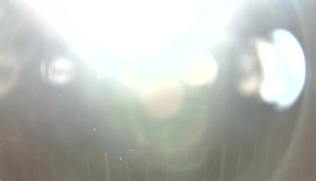 A bright, overexposed image with a white glare dominating the center. There are some indistinct shapes and colors in the background, but the details are unclear due to the lighting. A faint grid pattern is visible at the bottom of the image.