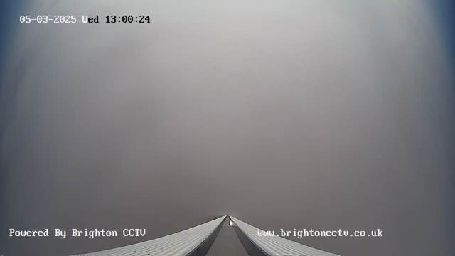 A foggy scene captured from a webcam, focusing on a long, narrow structure leading towards the horizon. The sky is obscured by gray mist, making visibility limited. The time and date at the top indicate it is Wednesday, March 5, 2025, at 1:00 PM. The bottom displays a watermark for Brighton CCTV.