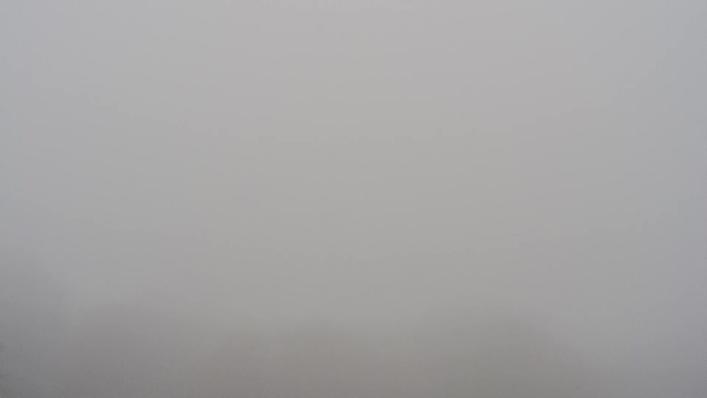 A gray and foggy scene where visibility is very low. The background is indistinct, blending into the fog, and there are no significant shapes or features visible. The overall atmosphere is dull and muted, creating an impression of overcast weather with dense fog.