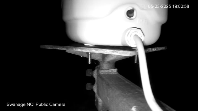 A close-up view of a white container, possibly a tank or a bucket, sitting on a metallic platform. Below the platform, there are visible screws or bolts securing the structure. A white cable is attached to the container, suggesting a connection to a power source. The overall image is dark, with limited visibility of the background, highlighting the outlined shapes of the objects in the foreground. The date and time displayed at the top right corner indicate March 5, 2025, at 7:00 PM.