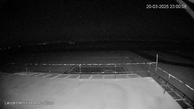 A dark, nighttime view from a webcam at Leicestershire Aero Club. In the foreground, there is a rooftop with a guardrail running along the edge. The background is mostly dark, with faint lights visible in the distance, suggesting a rural or semi-urban setting. No significant landmarks or features are discernible in the low light. The date and time stamp indicates it is March 20, 2025, at 11:00 PM.