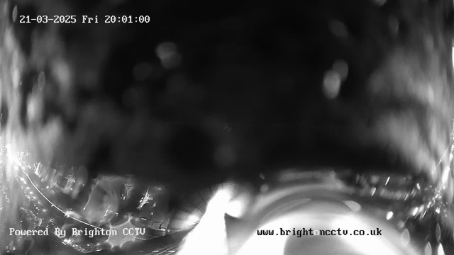 A blurred, low-contrast image taken from a webcam at night. The date and time displayed at the top indicate it is March 21, 2025, at 20:01. The bottom left corner contains the text "Powered By Brighton CCTV," and the bottom right corner shows the website "www.brightoncctv.co.uk." The image appears to be poorly lit with indistinct shapes, possibly indicating lights or reflections.