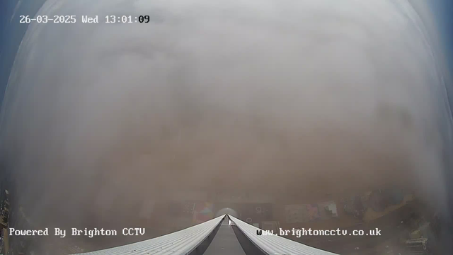 A webcam view shows a cloudy and foggy atmosphere, limiting visibility. The image is mostly made up of grayish-white clouds, with a slight gradient towards the top reflecting a hint of blue sky. Below, a peak of a rooftop or structure is visible in the foreground, leading into the cloudy backdrop. The timestamp indicates the image was captured on March 26, 2025, at 1:01 PM.