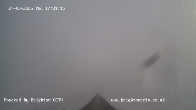A view of a foggy scene with limited visibility. The foreground features a dark shape that might outline a path or structure, fading into a gray, misty background. The date and time are displayed in the top left corner, and there is a watermark for "Brighton CCTV" at the bottom.