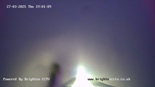 A blurry, low-light image showing a faint bright light in the center against a dark, hazy background. The time displayed is 19:01:09 on March 27, 2025, with a watermark at the bottom indicating "Powered By Brighton CCTV" and a website link.