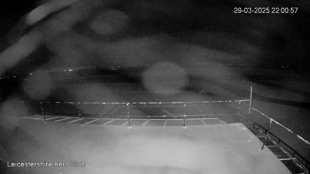 A dark and unclear scene showing a flat surface with faint outlines of a railing in the foreground. The background features indistinct shapes suggesting a distant horizon, with a few dim lights visible. The image is monochromatic, likely due to low light conditions. A timestamp indicates the date and time of the image as March 29, 2025, at 10:00 PM. The text "Leicestershire Aero Club" is positioned at the bottom of the image.