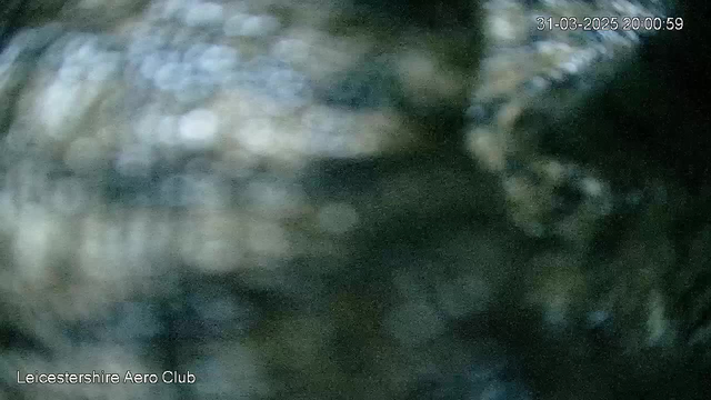 A blurry webcam image with indistinct shapes and colors, featuring dark and light spots that suggest movement or variation in texture. The timestamp at the top right reads "31-03-2025 20:00:59," and text at the bottom left indicates "Leicestershire Aero Club." The overall image appears unclear and lacks specific details.