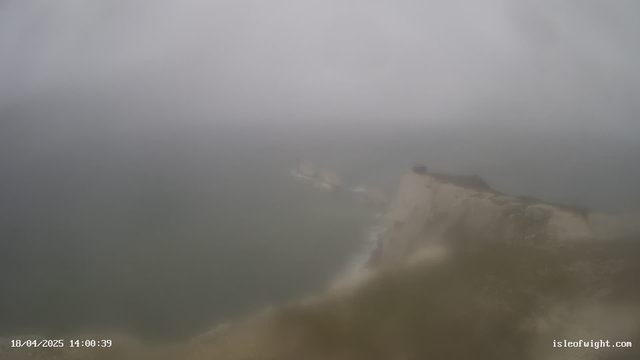 A foggy and blurred view of a coastal landscape. The image shows a rocky cliff edge overlooking a gray, turbulent sea. The sky is overcast, and visibility is limited due to fog. The date and time displayed in the corner indicate April 18, 2025, at 2:00 PM.