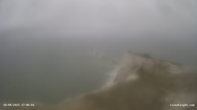 A foggy coastal scene with grey skies and rough waters. The horizon merges with the mist, making it difficult to distinguish the sea from the sky. Waves crash against a rocky shoreline, adding a sense of motion to the image. The visibility is low, creating an atmospheric and moody landscape. A timestamp at the bottom indicates the date and time as 18/04/2025, 17:00:01.