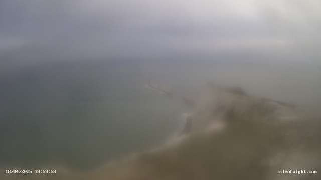 A blurry image of a coastal scene, with grey and cloudy skies above and dark waters below. In the distance, a faint outline of a boat can be seen on the water, and there are some waves breaking near the shore. The overall atmosphere is overcast, creating a muted and indistinct view of the landscape. A timestamp at the bottom indicates the date and time.