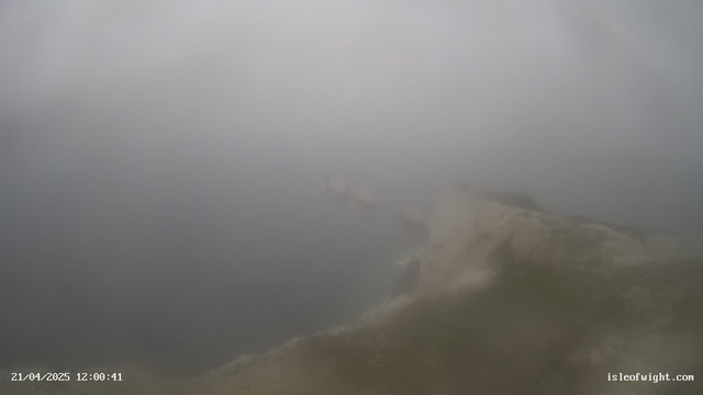 A hazy landscape with fog obscuring visibility. The image shows a rocky shoreline on the right side, leading towards a body of water. Portions of the water are visible, but details are unclear due to the fog. The date and time at the bottom indicate April 21, 2025, at 12:00:41.