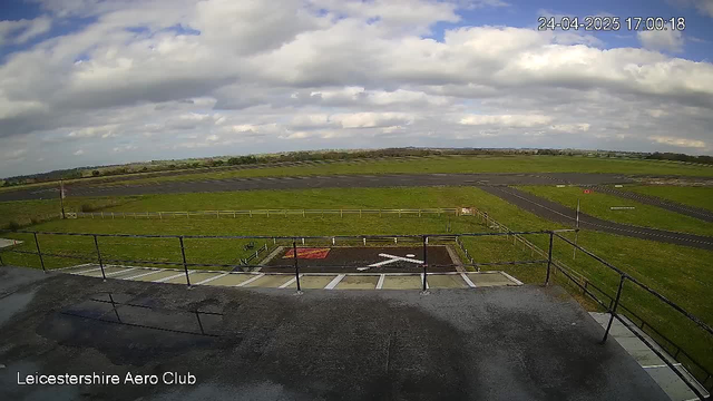 A view from a webcam overlooking an open field and sky filled with clouds, with a small parking area and railing in the foreground. The location is indicated as Leicestershire Aero Club, and the timestamp shows the date and time as 24-04-2025, 17:00:18.