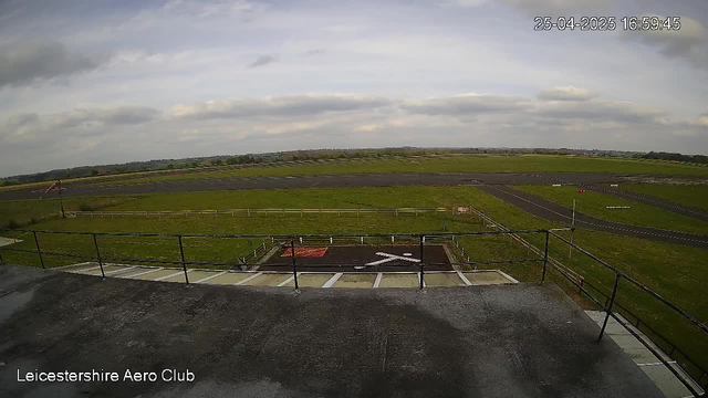 A view from a webcam at Leicestershire Aero Club showing an overcast sky with some clouds, a grassy airfield with runways and taxiways, a helipad with a white helicopter symbol, and a caution sign on the ground. The timestamp in the upper right corner indicates the date and time as 25th April 2025 at 16:59:45.