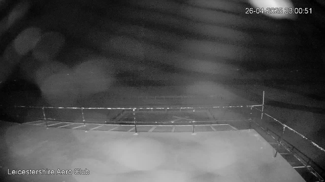 A black and white webcam image shows the outside of the Leicester Aero Club building at night. The sky is cloudy, and there are no visible lights or activity. The timestamp in the top right corner reads "26-04-2025 23:00:51". The name "Leicestershire Aero Club" is displayed in the bottom left corner.
