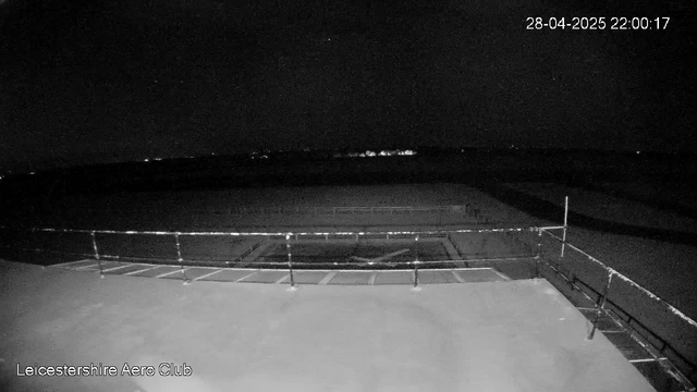 A black-and-white image captured by a webcam showing a large, empty outdoor sports pitch at night. The pitch is surrounded by a metal fence, and there are no people or animals visible. The sky is dark with a few faint stars. The timestamp in the top right corner reads "28-04-2025 22:00:17," and "Leicestershire Aero Club" is written in the bottom left corner.