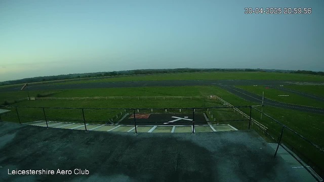 An empty rooftop viewing platform overlooking a green airfield with runways and grassy areas. The image shows a clear evening sky, with the date and time in the top right corner, and "Leicestershire Aero Club" written in the bottom left corner.