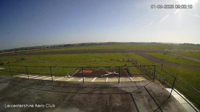 An outdoor scene at a small airport with a runway extending into the distance, grassy fields on both sides, and a clear blue sky. The image is timestamped "01-05-2025 09:00:10" and has a label in the bottom left corner that reads "Leicestershire Aero Club."