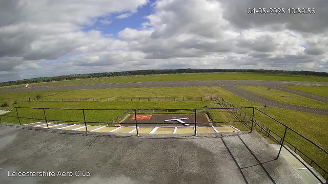 An outdoor view from a webcam showing a runway and grassy fields under a partly cloudy sky. The timestamp in the top right corner reads "04-05-2025 10:59:56" and "Leicestershire Aero Club" is indicated in the bottom left corner.