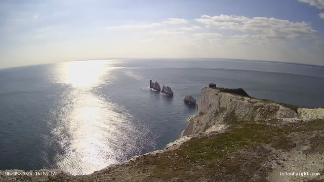 A view from a cliff overlooking the ocean during the day. The sunlight reflects off the water, creating a bright glare. Several large rock formations are visible in the water near the base of the cliff, and there are a few clouds scattered across the blue sky. The date and time in the corner indicate it was taken on June 5, 2025, at 4:59 PM.
