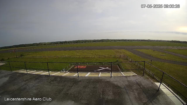A view from a webcam showing an airfield with runways and grassy areas. The sky is partly cloudy, and the lighting suggests it is early morning. The timestamp in the top right corner reads "07-05-2025 09:00:28." In the bottom left corner, there is text that says "Leicestershire Aero Club." The scene is calm and open, with no aircraft visible.