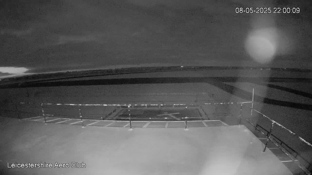 A black and white image captured by a webcam showing an empty outdoor area with a railing and a circular structure in the center. The sky appears cloudy or overcast, and the scene is dimly lit, likely during nighttime. The timestamp reads 08-05-2025, 22:00:09. The location is indicated as Leicestershire Aero Club.