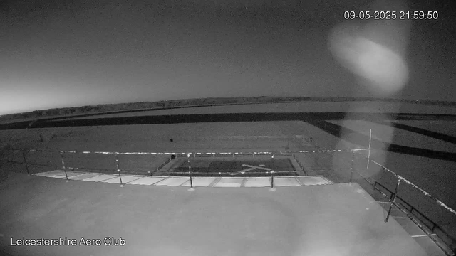 A black-and-white image from a webcam shows a wide view of an outdoor area at night, with a circular runway or helipad in the center surrounded by a railing. The scene is dark with minimal lighting, and the sky appears overcast or very dark. The timestamp in the top right corner indicates the date and time as 09-05-2025 at 21:59:50. The bottom left corner features the text "Leicestershire Aero Club."
