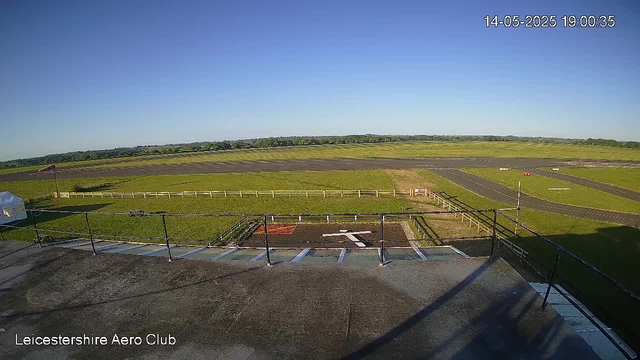 A clear view of an airfield with a runway and grassy areas under a bright blue sky. The image is captured from an elevated position, overlooking the tarmac and surrounding greenery. The weather appears sunny and calm. The timestamp shows the date and time as 14th May 2025 at 19:00:35. The text "Leicestershire Aero Club" is visible in the lower left corner.