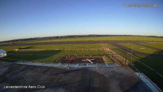 A wide view of an airfield on a clear day, with a grassy runway area, some small buildings, and a fence in the foreground. The sky is blue with no clouds visible. The timestamp in the top right corner indicates the date and time as May 14, 2025, at 8:00 PM and 44 seconds. The bottom left corner shows the text "Leicestershire Aero Club."