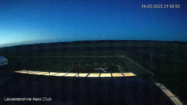 A dark outdoor scene at dusk or dawn showing a runway or helipad with a row of illuminated panels marking its edge. The sky is a deep blue transitioning to black with a faint glow on the horizon. The image has a timestamp in the upper right corner reading "14-05-2025 21:59:50," and "Leicestershire Aero Club" is written in the lower left corner. The setting appears to be part of an airfield or aviation facility.