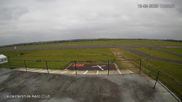 A view from a webcam overlooking an airfield with empty taxiways and runways in the distance, overcast sky with gray clouds, and the time and date displayed in the top right corner as 15-05-2025 14:00:50. The bottom left corner shows the text "Leicestershire Aero Club."