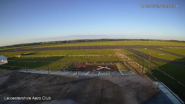 A wide view of an airfield shows clear blue sky, grassy areas, and some paved runways stretching into the distance. The foreground includes a rooftop or balcony with a railing, and the bottom left corner displays the text "Leicestershire Aero Club." The timestamp in the upper right corner indicates the date and time as 17-05-2025, 20:00:01.