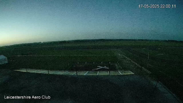 A view from a webcam showing an empty outdoor runway or tarmac area with a fence along the perimeter. The sky is transitioning from dusk to night, with a faint glow on the horizon. The image includes a timestamp of 17-05-2025 22:00:11 and a label in the bottom left corner reading "Leicestershire Aero Club."