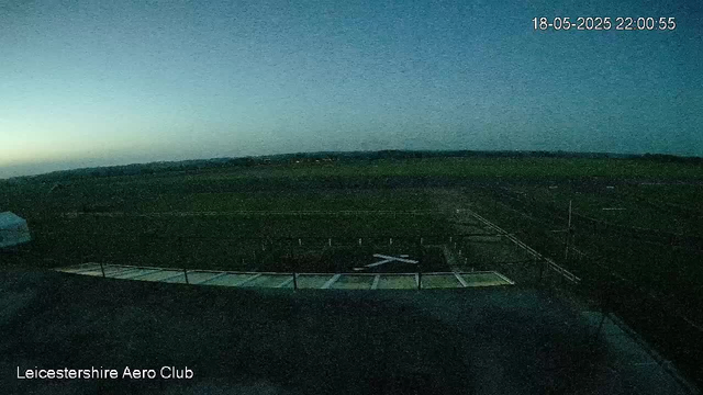 A view from a webcam showing an outdoor area at night or dawn, with a dark landscape and a faintly lit horizon in the distance. The sky is mostly dark, with a slight gradient indicating early morning or late evening light. In the bottom left corner, there is text that reads "Leicestershire Aero Club," and in the top right corner, there is a timestamp showing the date as 18-05-2025 and the time as 22:00:55.