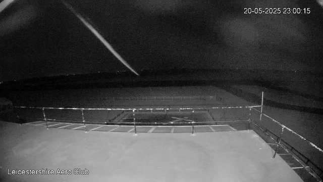 A black-and-white image from a webcam shows an empty outdoor sports field enclosed by a fence. The sky is dark, indicating nighttime, and some stars are faintly visible. The date and time in the upper right corner read "20-05-2025 23:00:15." The bottom left corner has the text "Leicestershire Aero Club."