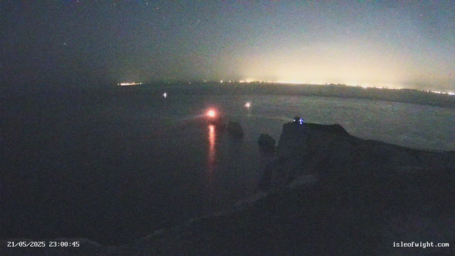 A nighttime scene over the ocean with a dark sky and distant city lights illuminating the horizon. Several small boats are visible on the water, with a few faint lights on their decks. The timestamp at the bottom left indicates the date and time as May 21, 2025, at 23:00:45.