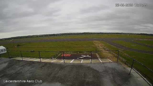 An outdoor view of a runway and surrounding green fields under a cloudy sky, with the timestamp "22-05-2025 12:00:55" in the top right corner and "Leicestershire Aero Club" written in the bottom left corner.