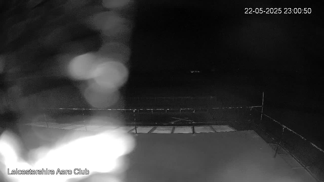 A black-and-white image captured by a webcam at night, showing the top of an aircraft or control tower with a railing or structure in the foreground. The background is dark, and the scene appears to be at Leicestershire Aero Club, with a timestamp in the top right corner indicating the date and time as 22-05-2025 at 23:00:50.