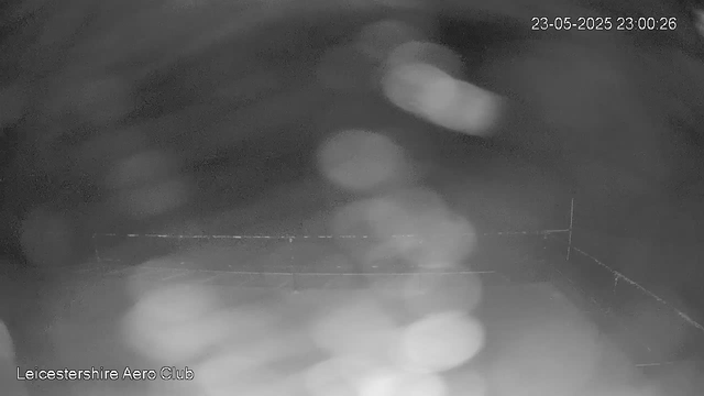 This is a black-and-white image from a webcam showing raindrops on the camera lens, creating blurry, circular light spots. The background appears dark and indistinct due to the rain and low light conditions. The image is timestamped "23-05-2025 23:00:26" and has the text "Leicestershire Aero Club" in the bottom left corner.