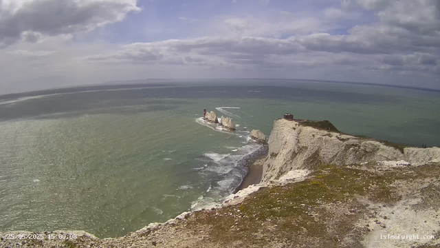 A view of white chalk cliffs along a coastline with a small building or observation post at the edge. In the sea, there are two large rock formations with a lighthouse on one of them. The sky is partly cloudy with patches of blue. The timestamp in the bottom left corner indicates the date and time as May 25, 2025, at 3:00 PM.